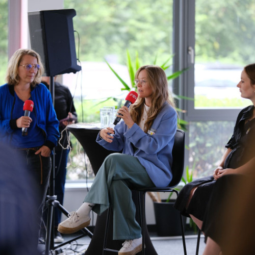 Rotes Mikrofon in der Hand und Sitzend auf einem Panel in blauem Blazer