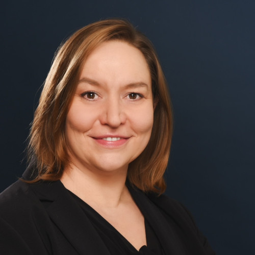 Portrait photo of a woman facing the camera, smiling, dark background, business attire.